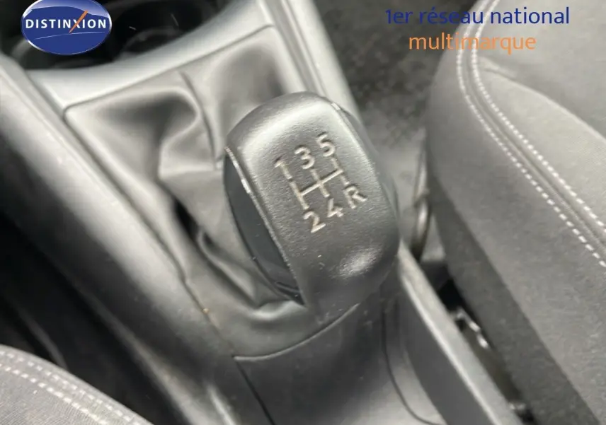 Gros plan sur le levier de vitesses manuel noir de la Peugeot 208 Société blanche, avec coutures visibles sur le siège tissu noir.
