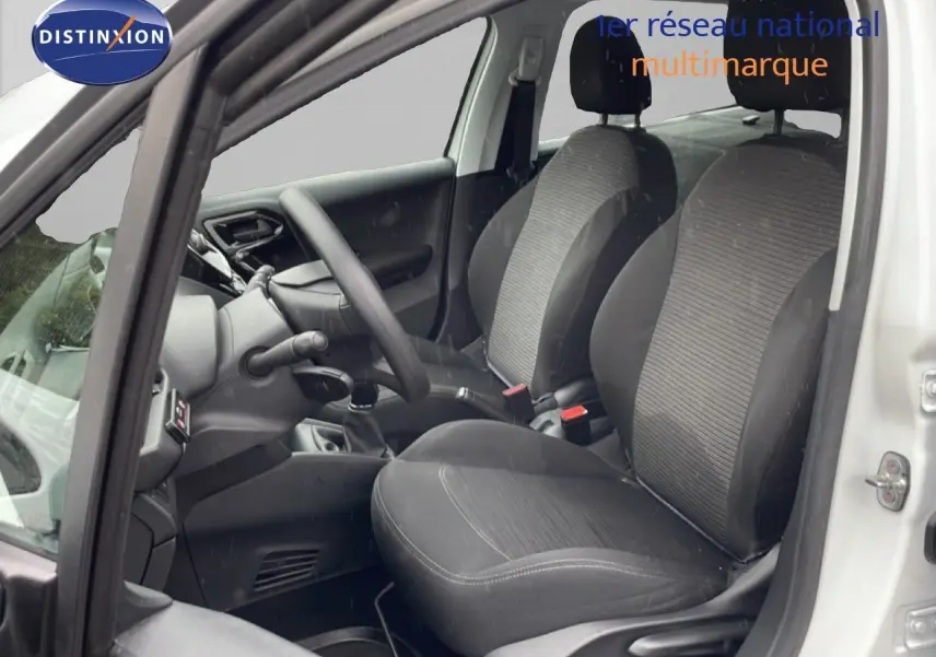 Vue intérieure côté conducteur de la Peugeot 208 Société blanche, montrant les sièges tissu noirs et le volant.