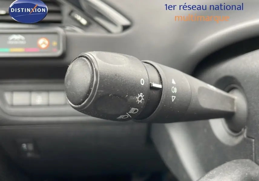 Gros plan sur la commande des phares à gauche du volant dans l’habitacle sombre d’une Peugeot 208 Blanc Banquise.