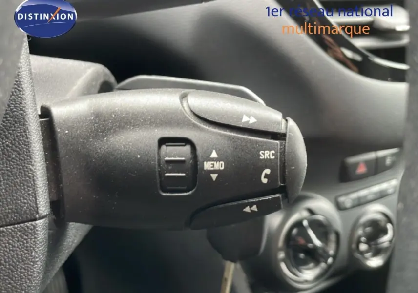 Gros plan sur la commande au volant de la Peugeot 208 Société blanche, avec tableau de bord et aérateurs en arrière-plan.