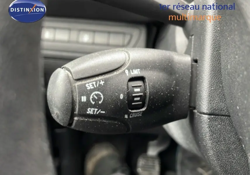 Gros plan sur la commande de régulateur de vitesse noire à gauche du volant d'une Peugeot 208 blanche banquise.