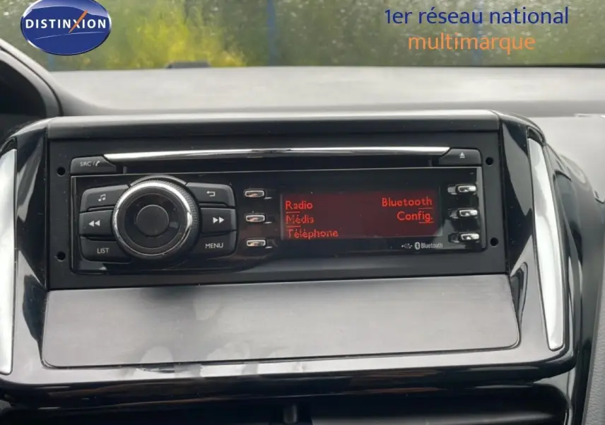 Gros plan sur la console centrale noire de la Peugeot 208 Société 2018, affichant l’écran radio avec options Bluetooth et média.
