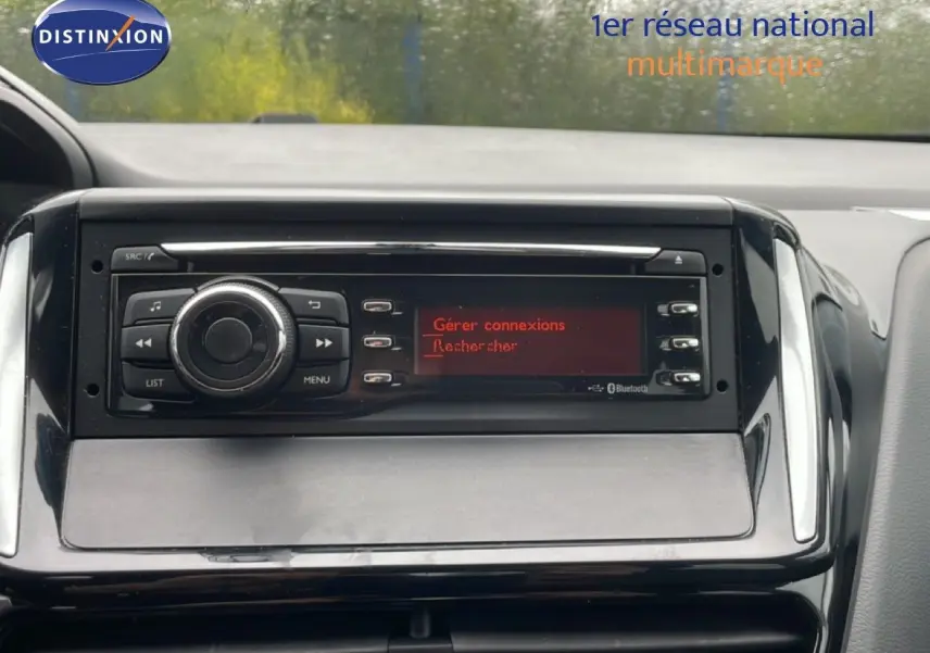 Vue rapprochée du tableau de bord de la Peugeot 208 Société blanche, mettant en valeur l’autoradio avec écran rouge et commandes.