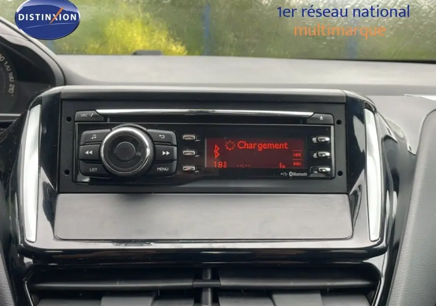 Gros plan sur la console centrale de la Peugeot 208 Société blanche, affichant l'autoradio avec écran rouge en mode Bluetooth.
