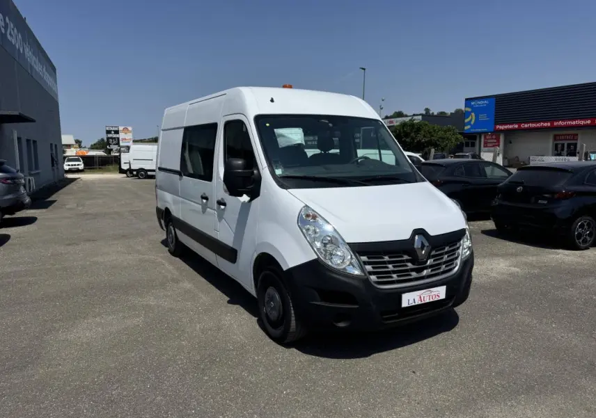Renault Master blanc en vue 3/4 avant droit sur parking, avec calandre noire et logo Renault visible.