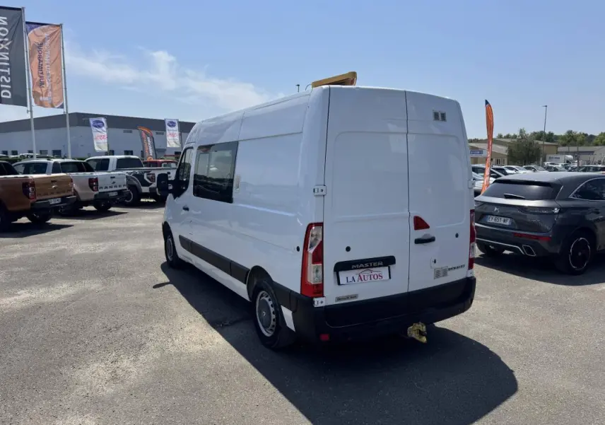 Renault Master blanc vue 3/4 arrière droit, fourgon utilitaire avec attelage et fenêtres latérales teintées.