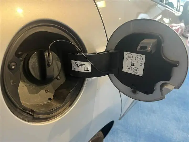 Bouchon de réservoir essence ouvert sur le côté gauche d'une Renault Clio IV gris argent, montrant les consignes de carburant.