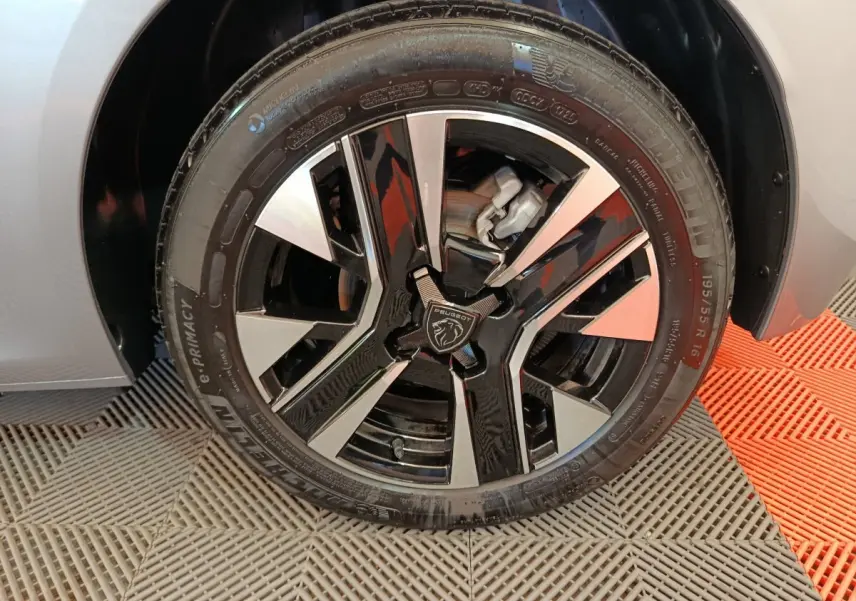 Gros plan sur la jante alliage noire et argentée du côté avant gauche d'une Peugeot 208 gris clair 2025.