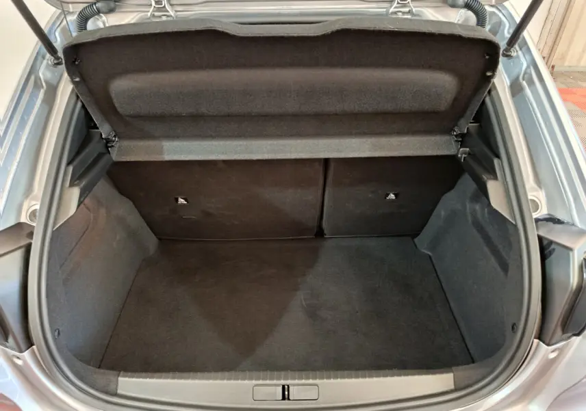 Coffre ouvert vu de l'arrière d'une Peugeot 208 gris clair, montrant l'espace de rangement et la tablette arrière.