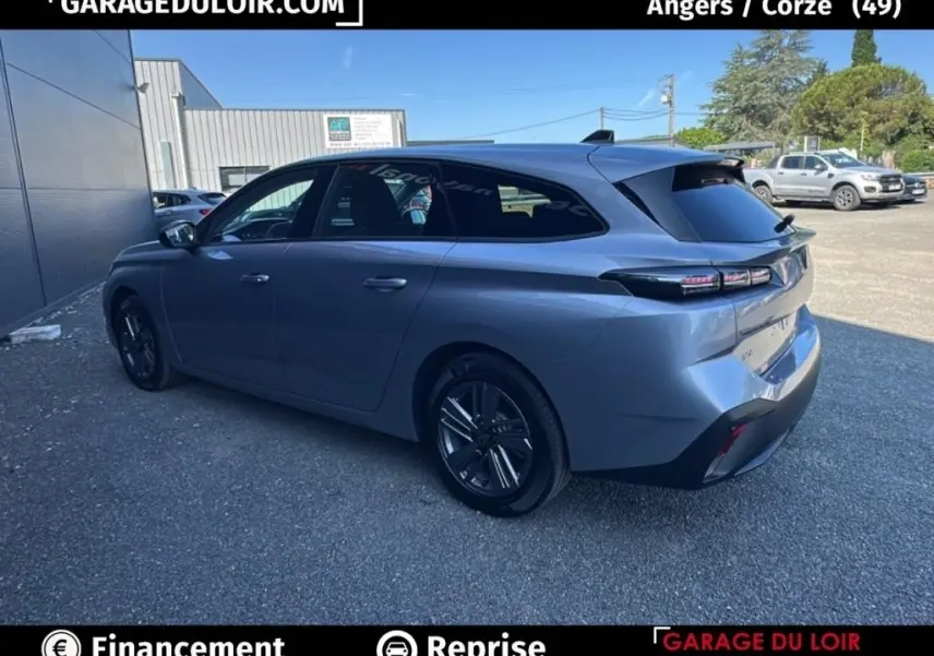 Vue 3/4 arrière droite d'une Peugeot 308 gris clair 2023 avec feux LED et carrosserie break élégante.