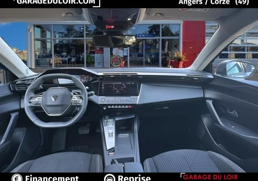 Vue intérieure avant de la Peugeot 308 gris clair 2023, avec tableau de bord digital et volant cuir multifonctions.
