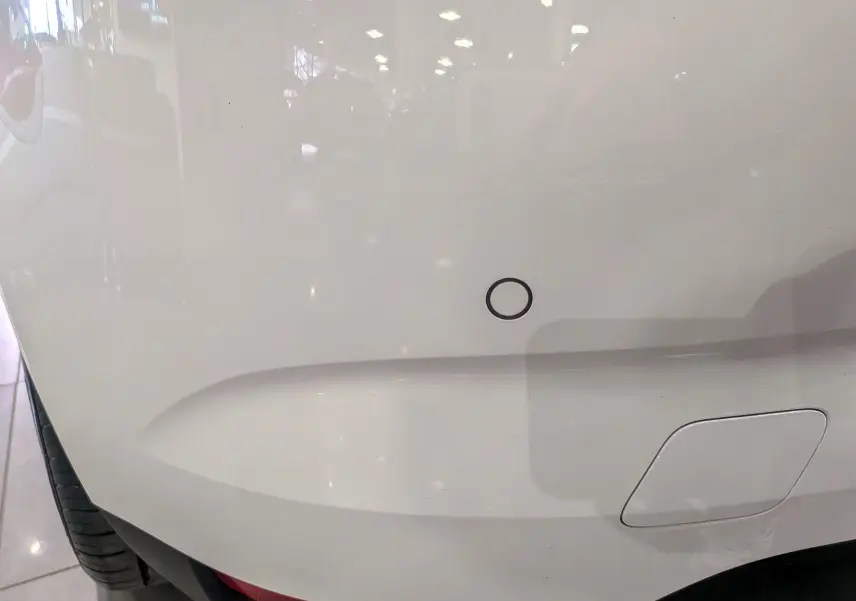 Détail du pare-chocs arrière blanc glacier de la Renault Mégane IV Berline avec capteur de recul circulaire visible.