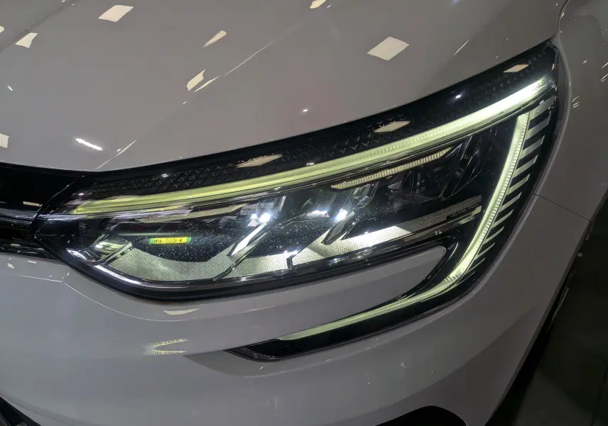 Gros plan sur le phare avant droit allumé de la Renault Mégane IV Berline Blanc Glacier, soulignant ses lignes LED distinctives.