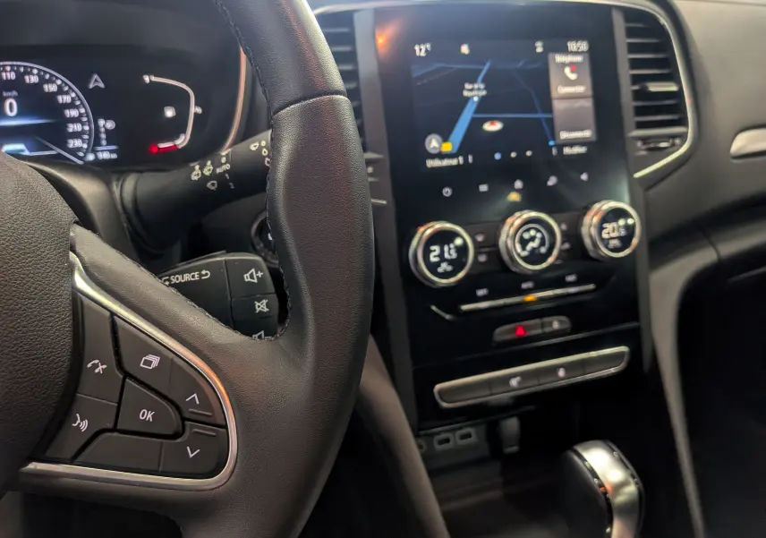 Vue intérieure de la Renault Mégane IV Berline, tableau de bord avec écran tactile et volant multifonction en cuir noir.