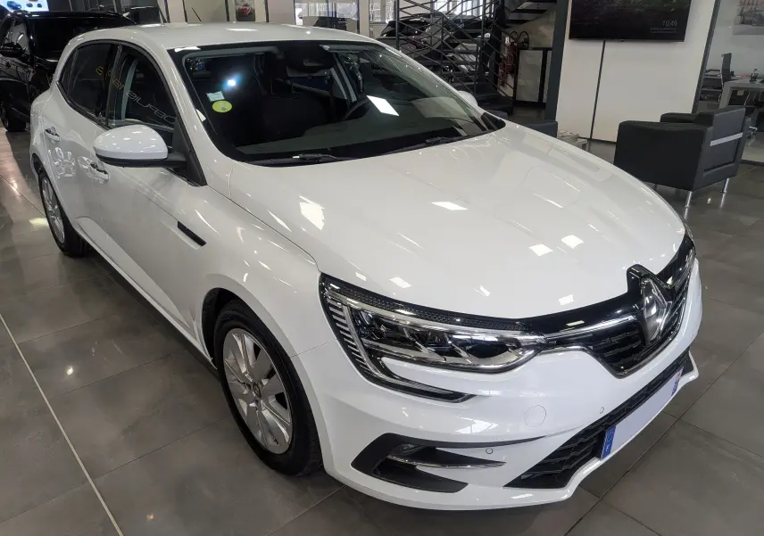 Renault Mégane IV Berline blanc glacier vue 3/4 avant droit en intérieur, avec phares LED et calandre noire brillante.