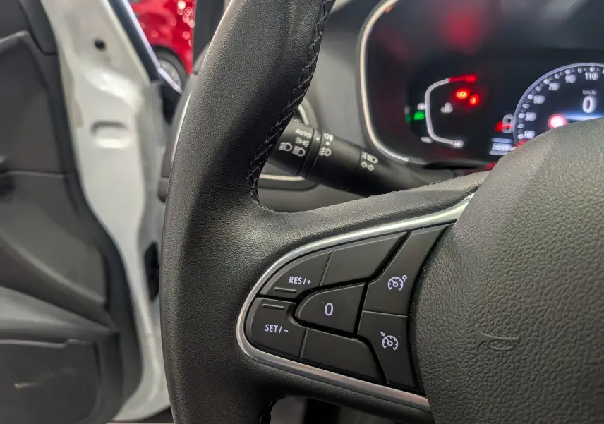 Gros plan sur le volant noir de la Renault Mégane IV Business, avec commandes de régulateur de vitesse visibles, porte ouverte blanc glacier.