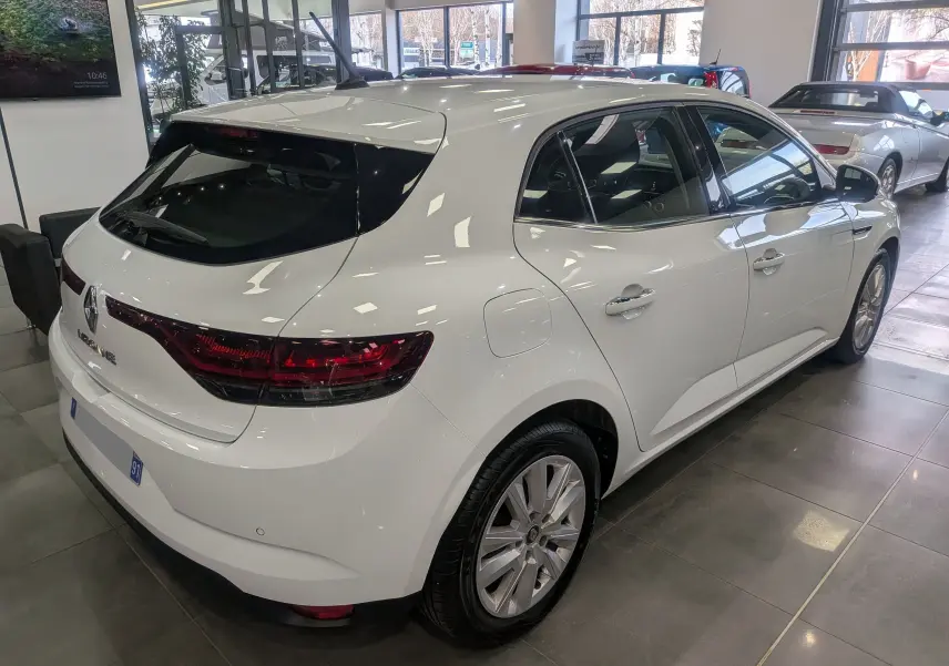 Renault Mégane IV Berline blanc glacier vue 3/4 arrière droit en intérieur, feux arrière LED et jantes alliage visibles.