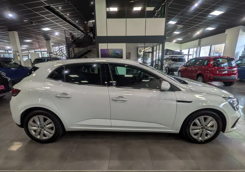 Vue de profil côté gauche d'une Renault Mégane IV Berline blanc glacier exposée en showroom, soulignant ses lignes épurées.
