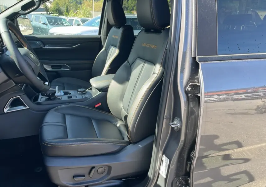 Vue intérieure côté conducteur du Ford Ranger gris carbone, sièges en cuir noir Wildtrak avec surpiqûres orange.