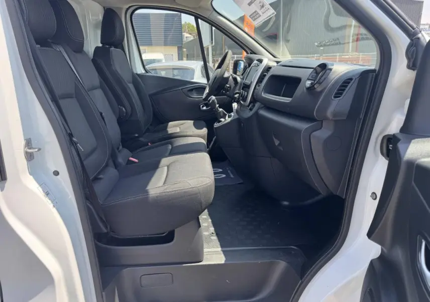 Intérieur du Renault Trafic Fourgon blanc 2019 vu côté droit, montrant les sièges avant et le tableau de bord noir.