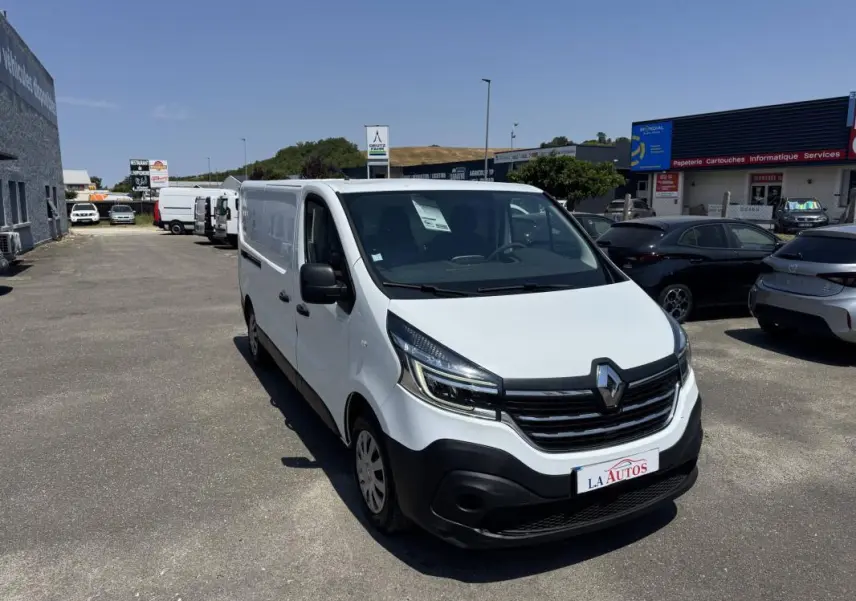 Renault Trafic Fourgon blanc vu en 3/4 avant droit sur un parking, avec calandre noire et phares modernes.