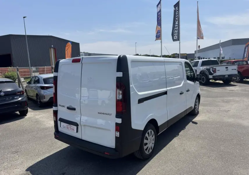 Vue 3/4 arrière droite d’un Renault Trafic Fourgon blanc stationné sur un parking extérieur.