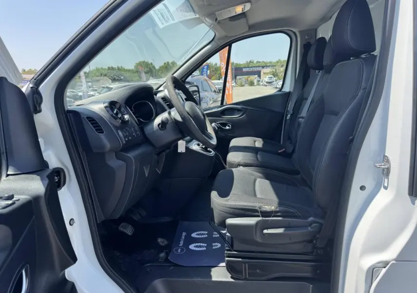 Vue intérieure côté conducteur du Renault Trafic Fourgon blanc 2019, montrant les sièges avant et le tableau de bord.