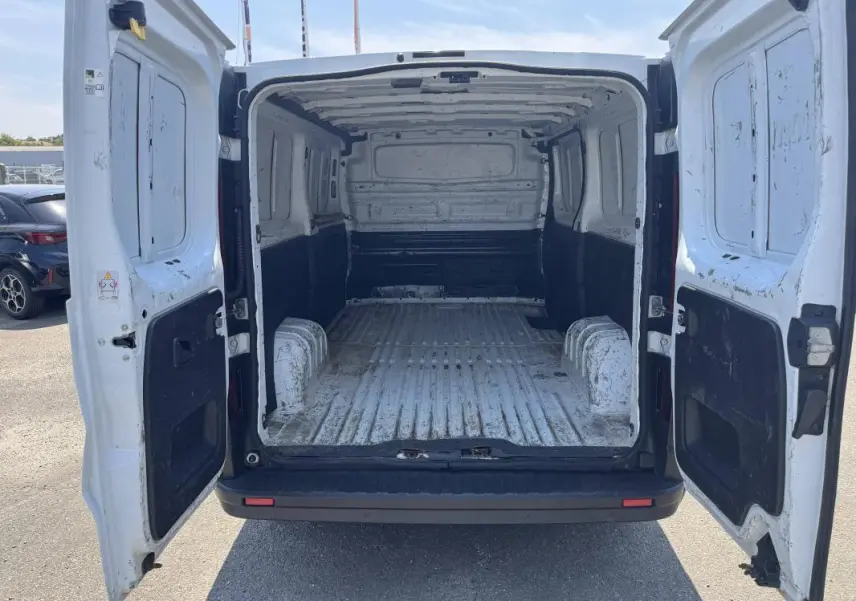 Vue arrière du Renault Trafic Fourgon blanc 2019 avec portes ouvertes montrant l’espace de chargement vide et usé.