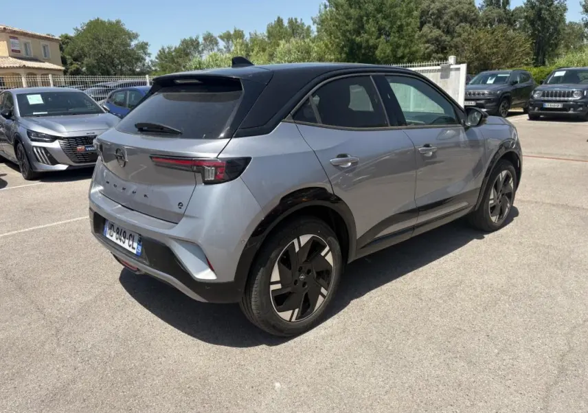 Opel Mokka électrique gris en 3/4 arrière droit, avec toit noir et jantes alliage 17 pouces, stationné en extérieur.
