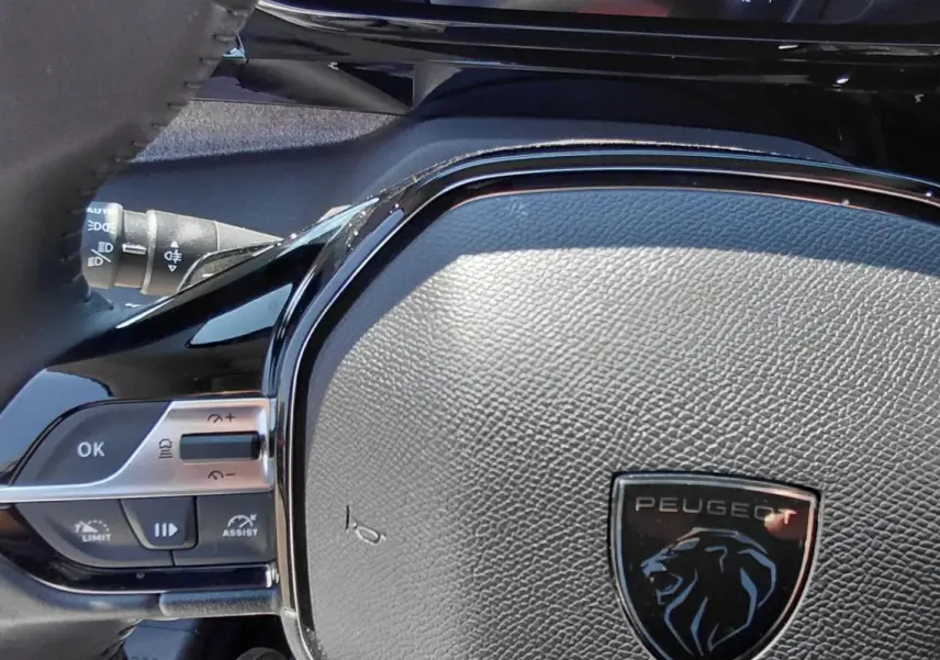 Gros plan sur le volant noir texturé du Peugeot 308 SW Hybrid 145 Allure avec commandes intégrées et logo lion.