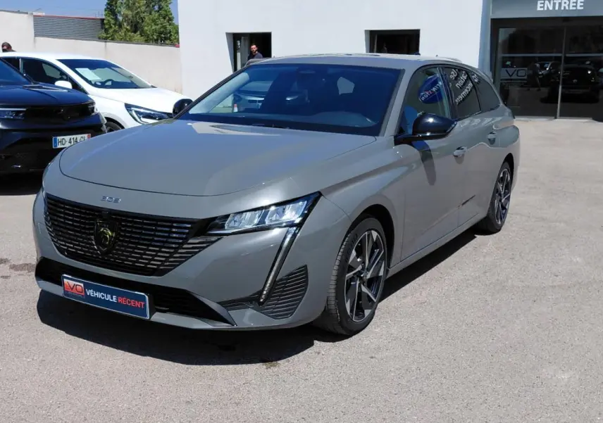 Peugeot 308 SW Hybrid gris vue 3/4 avant droit, avec calandre noire et jantes alliage 17 pouces visibles.