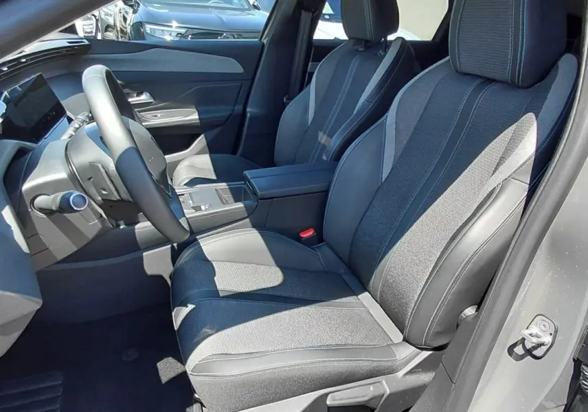 Vue intérieure côté conducteur du Peugeot 308 SW Hybrid gris 2025, montrant sièges tissu et cuir, volant et console centrale.