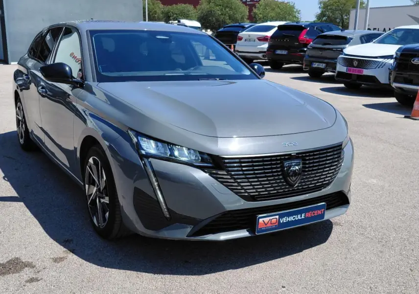 Peugeot 308 SW gris vue 3/4 avant droit, avec calandre noire distinctive et jantes alliage 17 pouces.