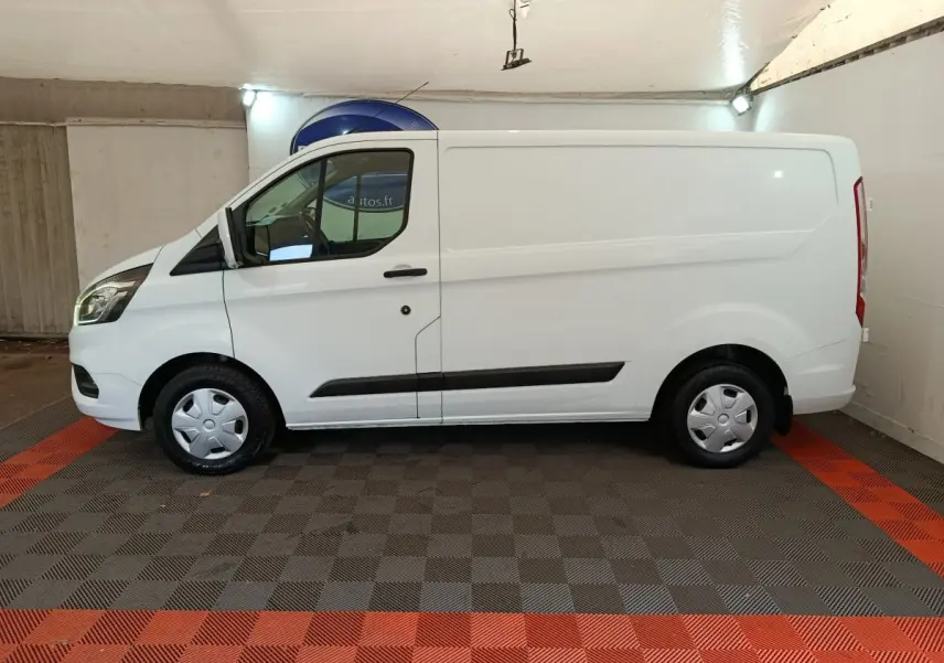 Vue de profil côté gauche d’un fourgon Ford Transit Custom blanc, avec jantes acier et habillage noir sur les bas de caisse.