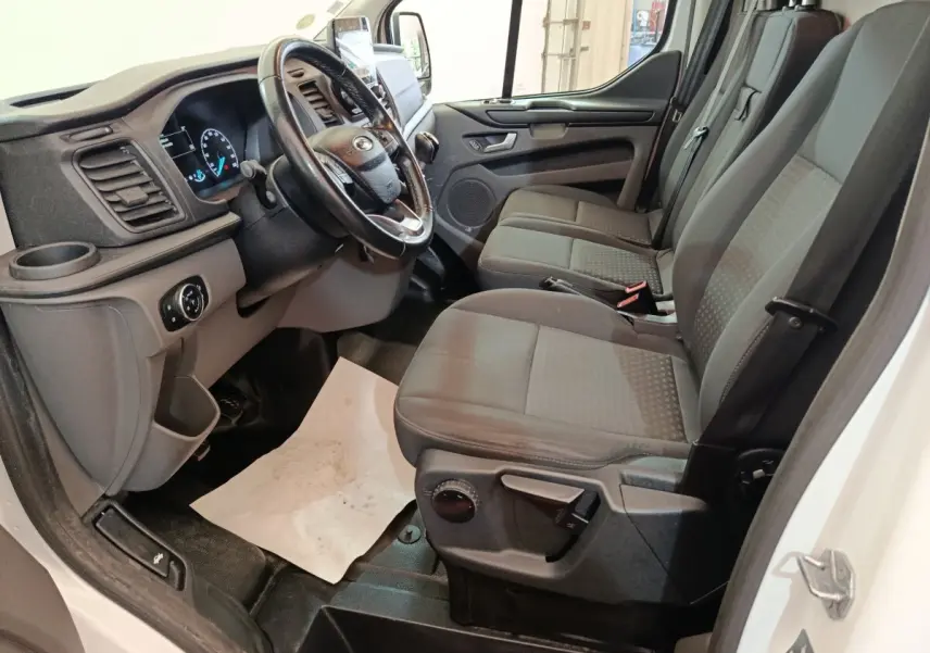 Vue intérieure côté conducteur du Ford Transit Custom blanc 2020, montrant le tableau de bord et la banquette avant grise.