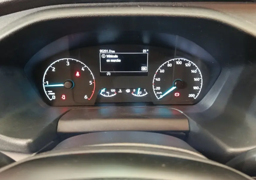 Vue rapprochée du tableau de bord numérique du Ford Transit Custom blanc, affichant 95 201 km et alertes actives.