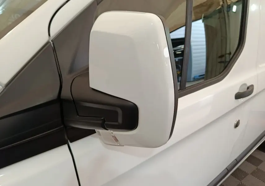 Gros plan sur le rétroviseur droit blanc du Ford Transit Custom Fourgon blanc, avec porte et poignée visibles en arrière-plan.