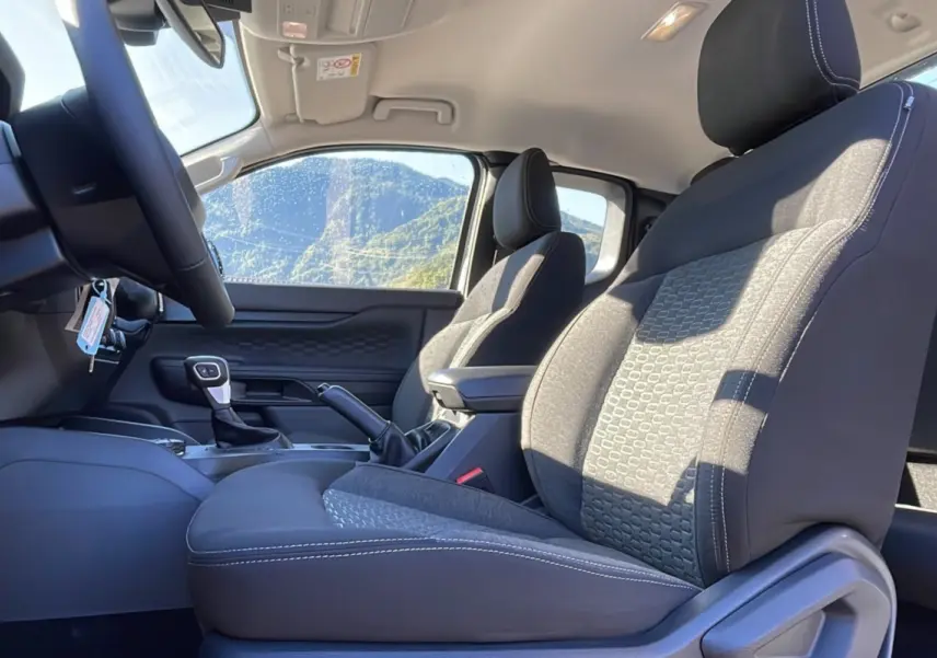 Vue intérieure côté conducteur du Ford Ranger 2026, sièges tissu gris avec surpiqûres blanches et accoudoir central.