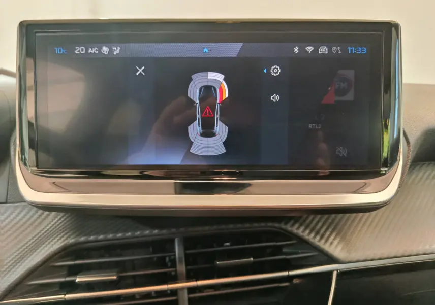 Écran tactile central de la Peugeot 208 PureTech 100 Allure 2025 affichant l'aide au stationnement en intérieur.