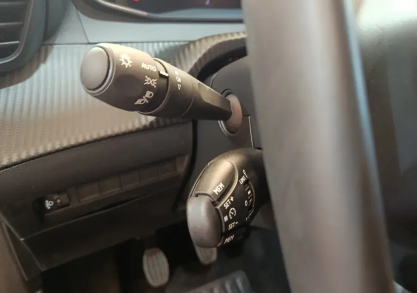 Gros plan sur les commandes au volant côté gauche du Peugeot 208 gris foncé, avec leviers de clignotant et régulateur de vitesse.