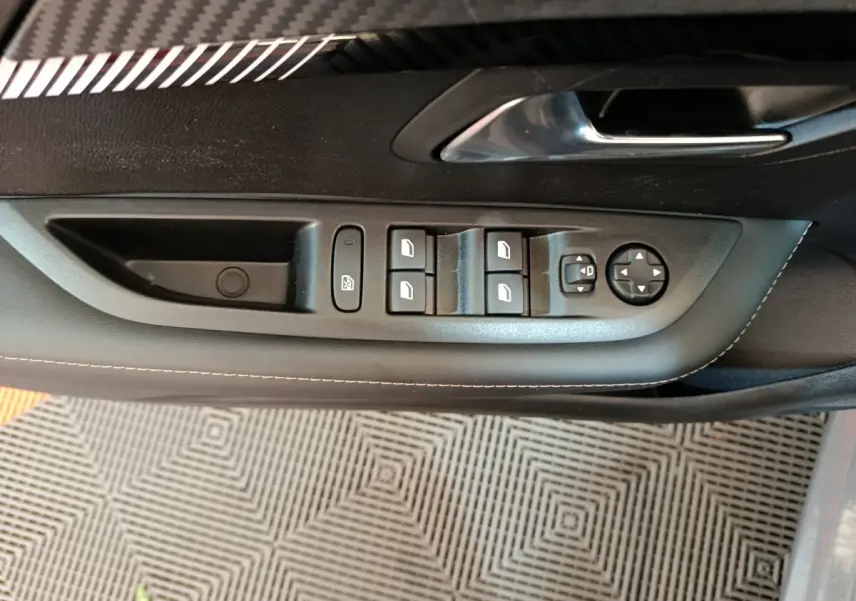 Panneau de porte côté conducteur de Peugeot 208 gris foncé avec commandes électriques des vitres et rétroviseurs.