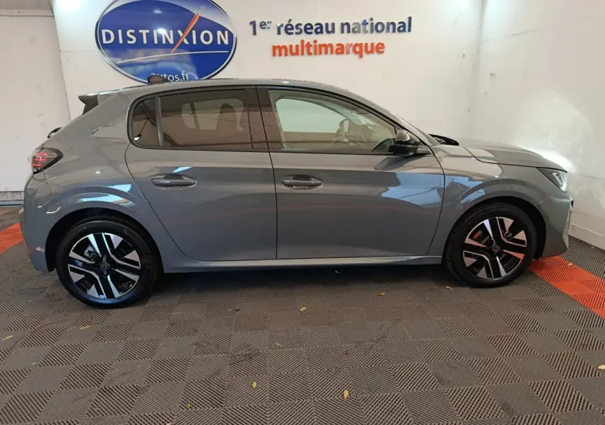 Profil côté droit d'une Peugeot 208 gris foncé 2025 avec jantes alliage et vitres teintées en intérieur showroom.