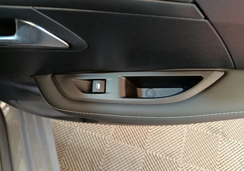 Détail de la poignée intérieure côté gauche en plastique noir avec bouton de lève-vitre sur Peugeot 208 gris foncé 2025.