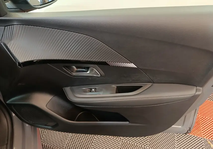 Intérieur côté gauche de la porte PEUGEOT 208 gris foncé avec insert effet carbone et commandes de vitre.