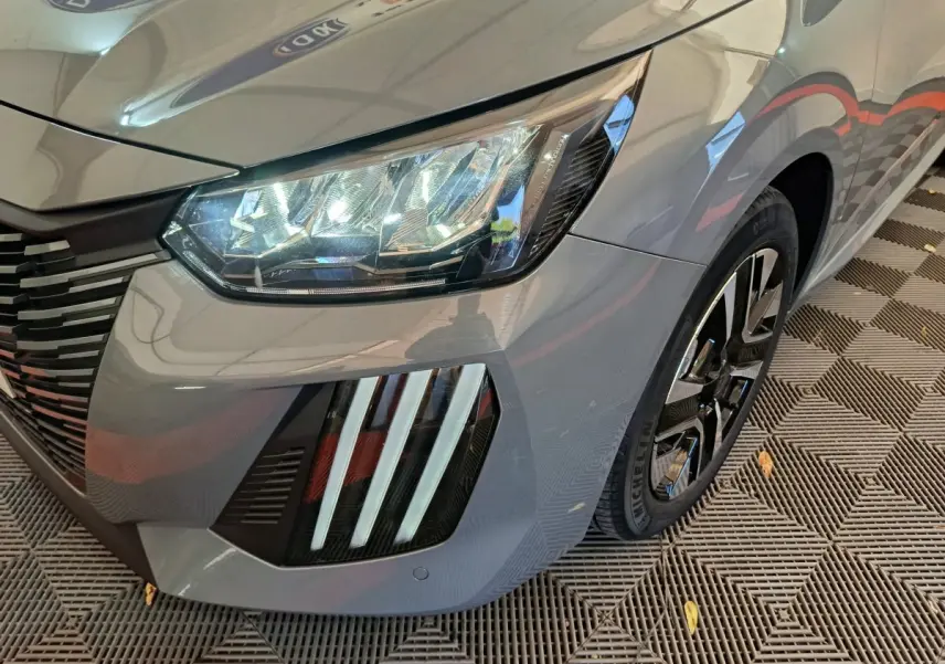 Gros plan sur l'avant droit gris foncé de la Peugeot 208 2025, mettant en valeur ses phares LED et jante stylisée.