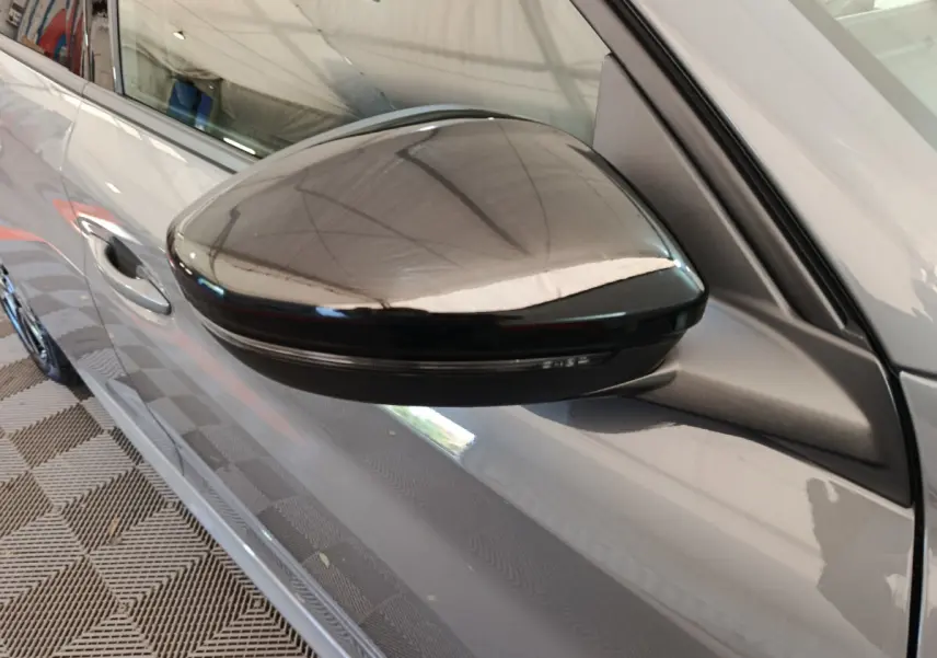 Rétroviseur noir côté gauche d'une Peugeot 208 gris foncé vue en gros plan sur porte avant.