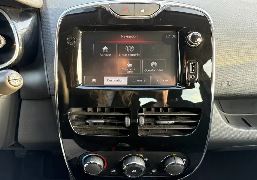 Vue rapprochée du tableau de bord noir brillant de la Renault Clio IV gris, avec écran GPS affichant le menu de navigation.