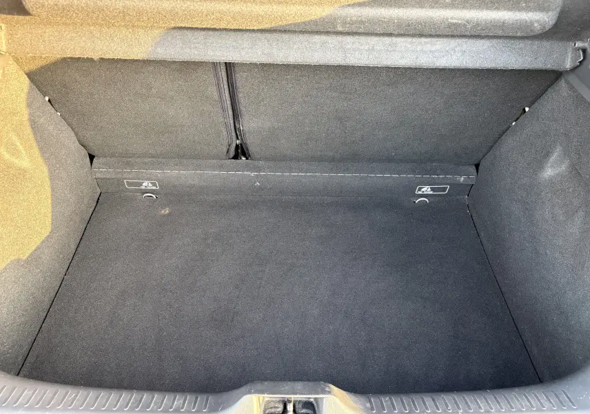 Coffre vide vu de face d’une Renault Clio IV gris, montrant la moquette noire et les fixations arrière.