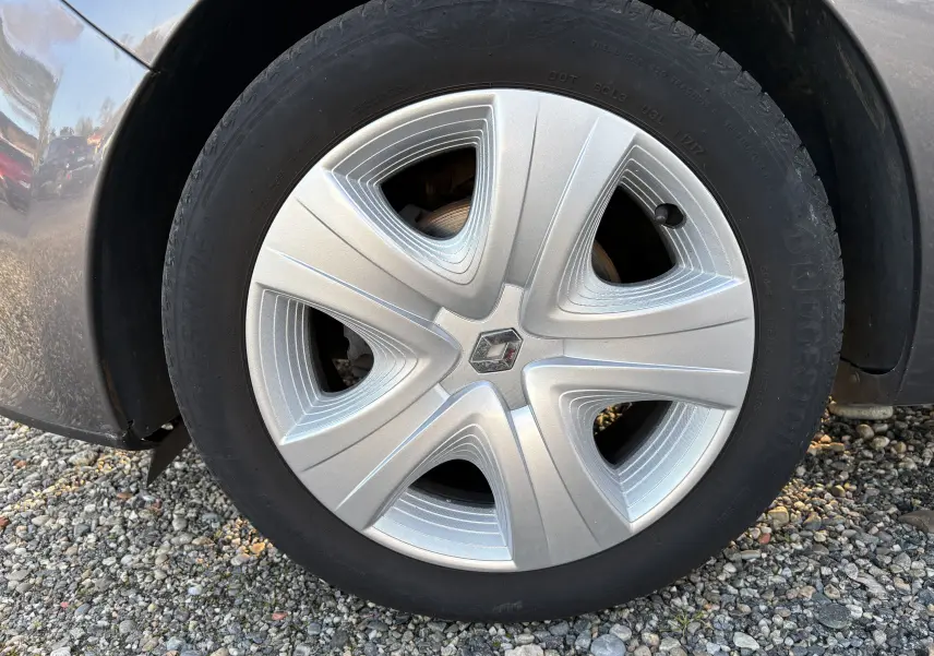 Vue rapprochée sur la roue arrière droite d'une Renault Clio IV gris métallisé garée sur un sol gravillonné.