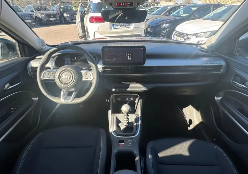 Vue intérieure avant du Jeep Avenger gris 2025, montrant le volant, tableau de bord digital et levier de vitesses manuel.